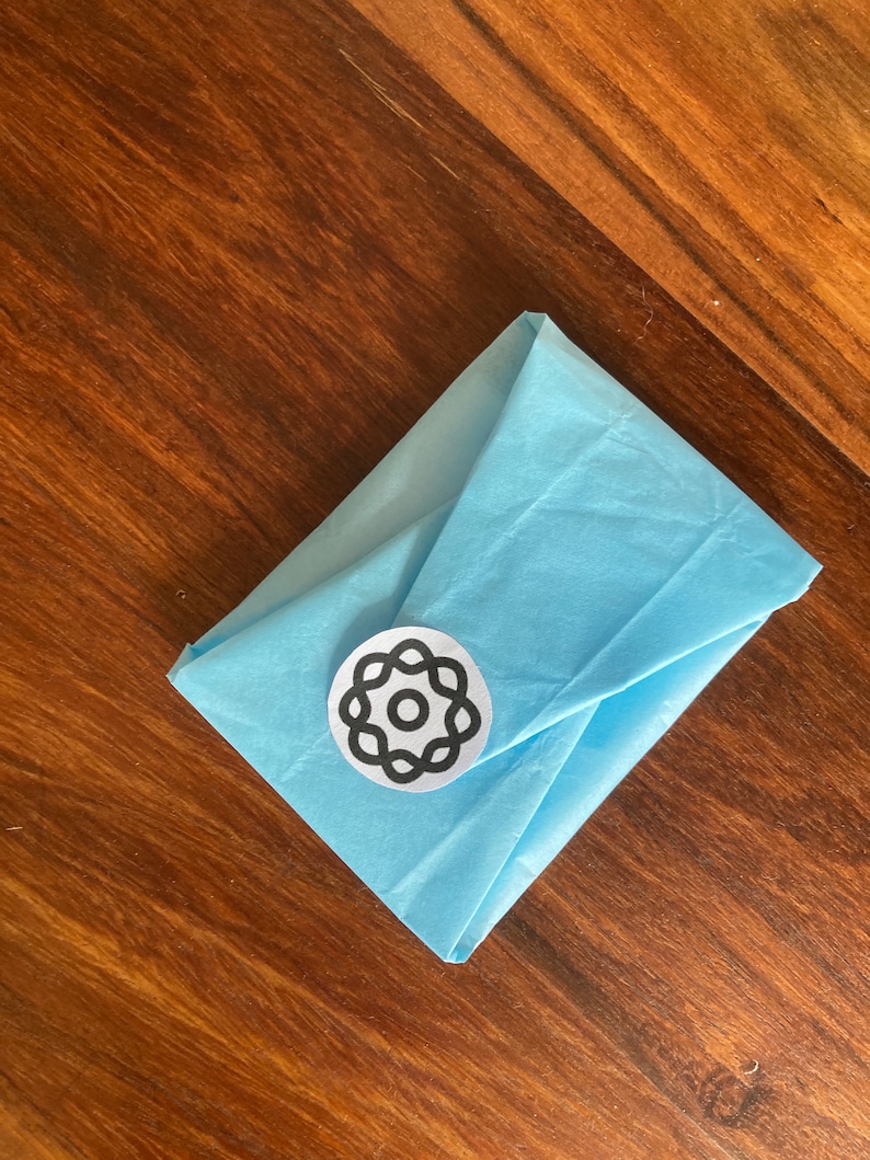 Peut inclure: Une enveloppe en papier de soie bleu clair avec un autocollant circulaire noir et blanc repr&eacute;sentant un motif stylis&eacute;.