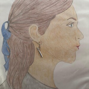 Peut inclure: Un dessin d'une personne aux cheveux bruns portant une boucle d'oreille en argent avec un design d&eacute;taill&eacute;. La boucle d'oreille est en forme de baguette.