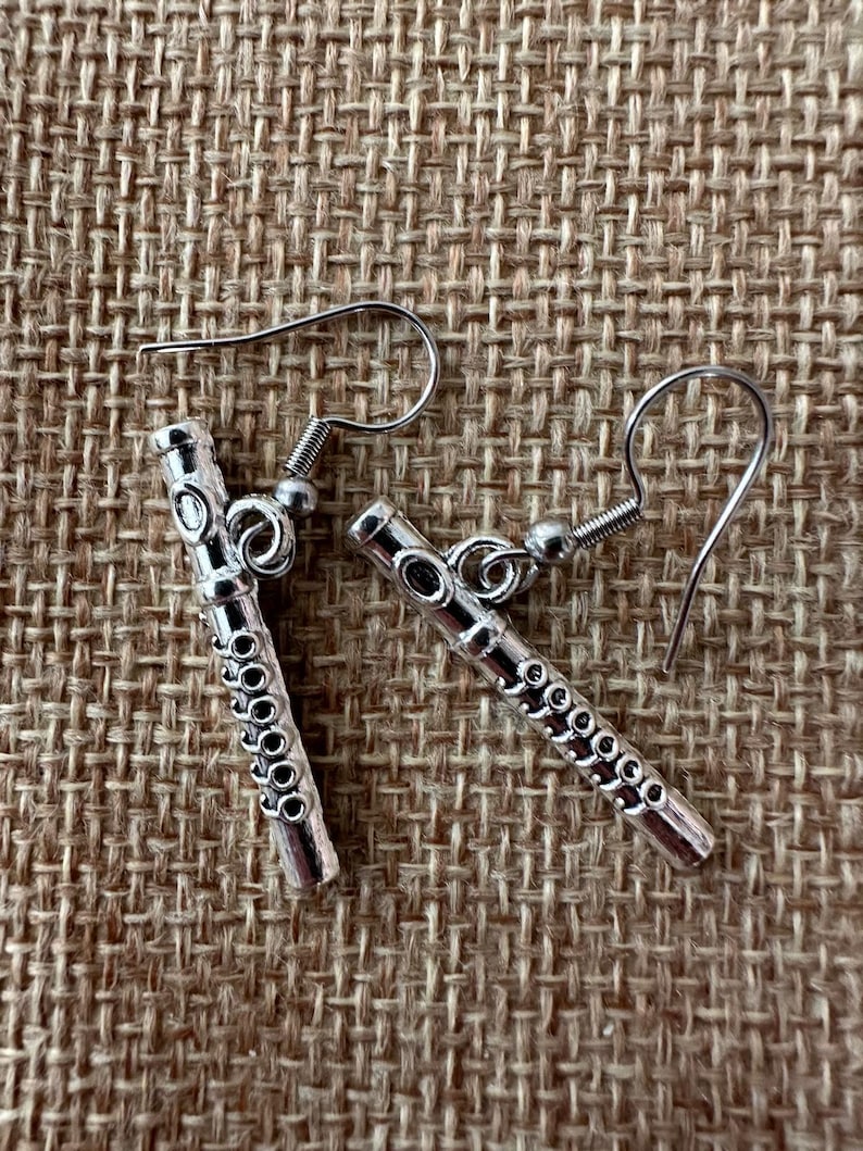Peut inclure: Une paire de boucles d'oreilles en argent en forme de fl&ucirc;tes. Les boucles d'oreilles ont un design d&eacute;taill&eacute; et sont suspendues &agrave; des crochets en argent.