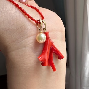 Op de afbeelding: Een rode koraal hanger ketting met een goudkleurige beugel en een cr&egrave;me-kleurige parel. De ketting heeft een delicate rode kralenketting. Het koraal heeft een takachtige vorm.