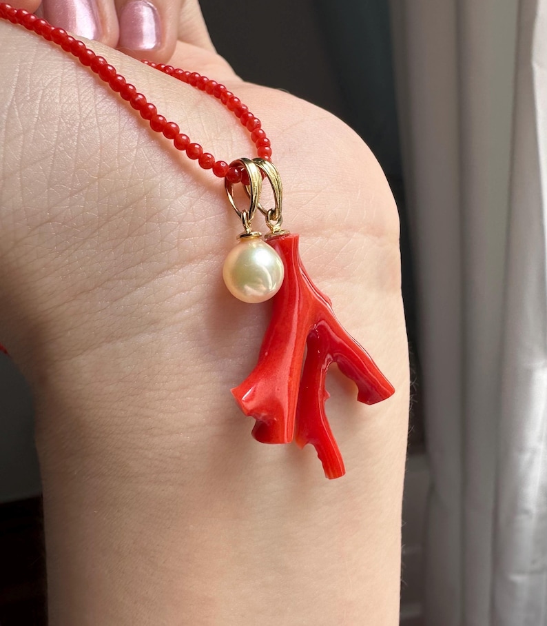 Op de afbeelding: Een rode koraal hanger ketting met een goudkleurige beugel en een cr&egrave;me-kleurige parel. De ketting heeft een delicate rode kralenketting. Het koraal heeft een takachtige vorm.