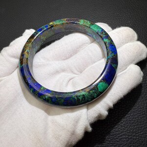 May include: A polished azurite and malachite bangle bracelet. The bracelet features a mix of deep blue, vibrant green, and brown hues. The gemstone bracelet is a circular shape and appears to be smooth to the touch.