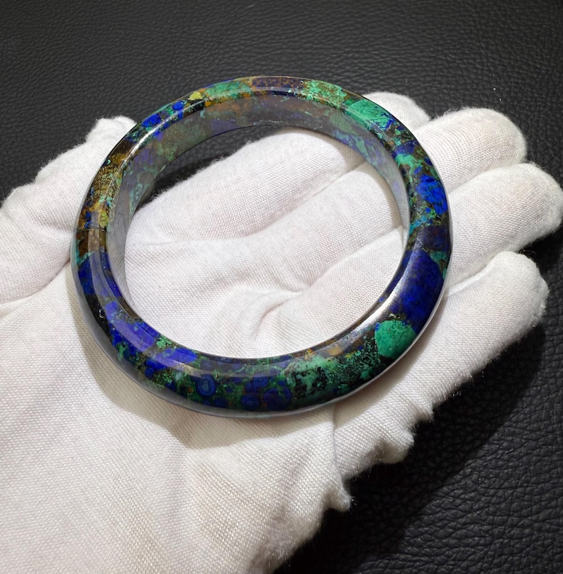 May include: A polished azurite and malachite bangle bracelet. The bracelet features a mix of deep blue, vibrant green, and brown hues. The gemstone bracelet is a circular shape and appears to be smooth to the touch.