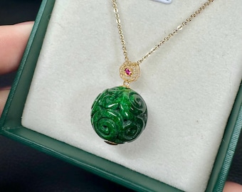May include: A gold necklace with a carved green jade pendant. The pendant is a sphere with intricate floral carvings. A small red gemstone is set in the gold clasp. The necklace is displayed in a green jewelry box.