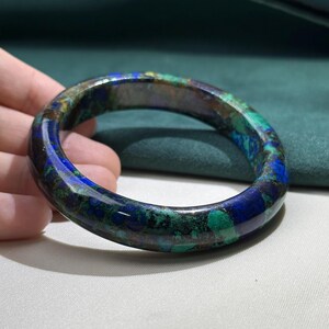 May include: A polished, round bracelet with a marbled appearance. The bracelet features a blend of deep blue, green, and brown hues. The gemstone bracelet is a unique piece of jewelry.