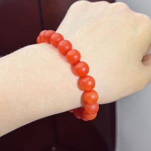 May include: A stretch bracelet composed of round, matte-finish orange beads. The beads are uniform in size and strung together on a flexible cord, creating a continuous circular shape that fits snugly around the wrist area shown in the image.