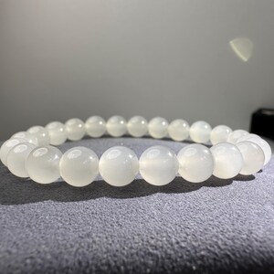 K&ouml;nnte beinhalten: Ein elastisches Armband bestehend aus glatten, runden, durchscheinenden wei&szlig;en Perlen mit einem dezenten opalisierenden Schimmer. Die Perlen sind einheitlich gro&szlig; und in einer durchgehenden kreisf&ouml;rmigen Schleife angeordnet.