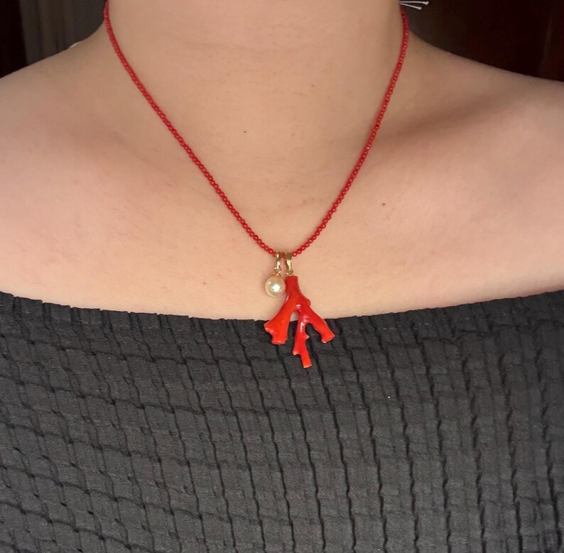 Op de afbeelding: Een rode koraal hanger ketting. De ketting heeft een delicate rode ketting met een koraaltak hanger en een kleine parel. Het koraal is felrood en de parel is wit. De ketting is een sieraad.