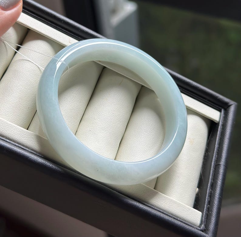 Pode incluir: Uma pulseira tipo bracelete de jade verde menta p&aacute;lido, lisa e polida, com uma apar&ecirc;ncia transl&uacute;cida e um perfil arredondado. A pe&ccedil;a de joalharia circular apresenta varia&ccedil;&otilde;es subtis na intensidade da cor e um acabamento brilhante.