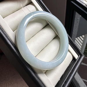 Pode incluir: Um bracelete de jade verde-p&aacute;lido, liso e transl&uacute;cido, com um perfil arredondado. Esta pe&ccedil;a de joalharia circular em pedra apresenta um acabamento polido e varia&ccedil;&otilde;es subtis de cor, exibindo um tom verde-menta suave ao longo da banda.
