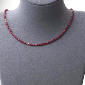 May include: A necklace composed of small, round, deep red beads strung together. The strand is accented with three small, polished gold-toned metal spacers placed at intervals along the length of the necklace, creating a subtle contrast.