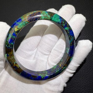 May include: A round bracelet with a marbled appearance. The bracelet features a mix of blue, green, and brown hues. The gemstone bracelet is a wearable accessory.