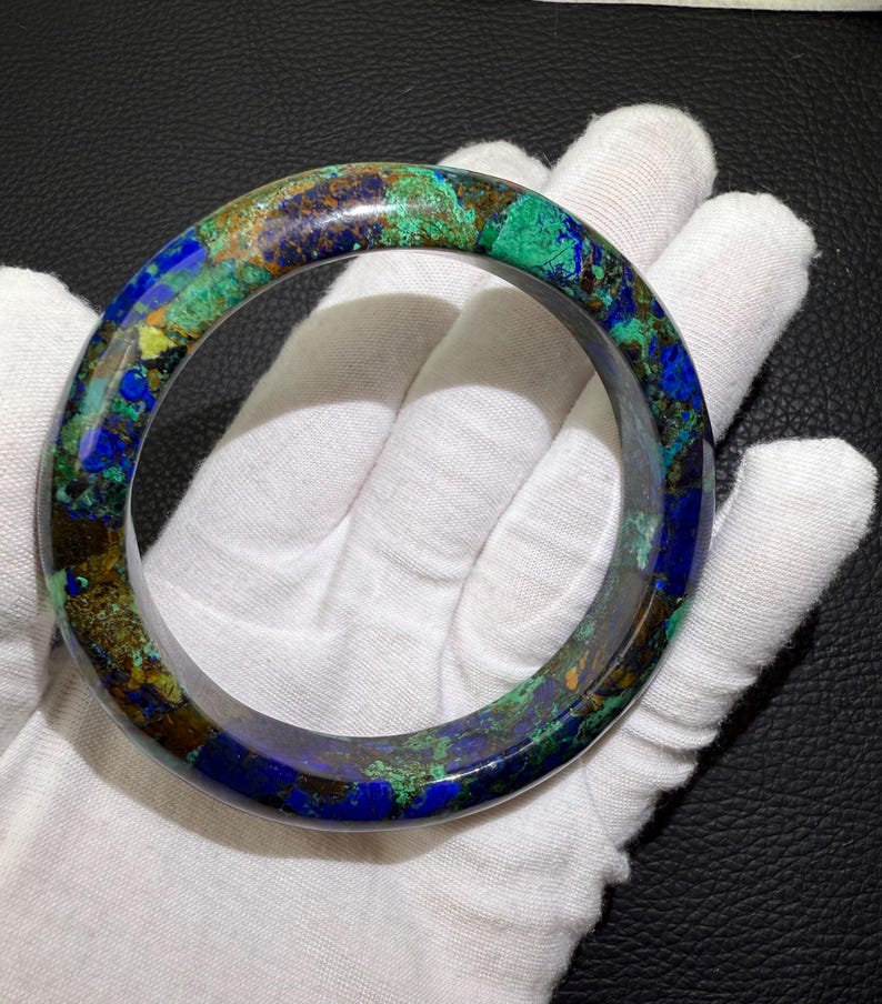 May include: A round bracelet with a marbled appearance. The bracelet features a mix of blue, green, and brown hues. The gemstone bracelet is a wearable accessory.