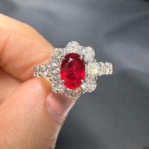 May include: A red ruby gemstone ring with a halo of small diamonds. The ring is set in white gold and has a delicate band.