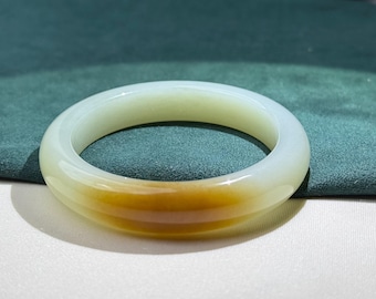 May include: A jade bangle bracelet with a smooth, polished surface. The bracelet transitions from a pale green to a warm, golden-yellow hue. The circular design is simple and elegant, suitable for everyday wear.