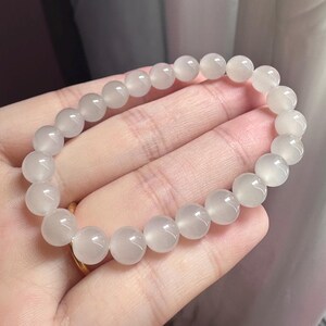 K&ouml;nnte beinhalten: Ein elastisches Armband aus glatten, runden, halbtransparenten wei&szlig;en Perlen mit einem sanften, milchigen Glanz. Die Perlen sind einheitlich gro&szlig; und zu einer durchgehenden kreisf&ouml;rmigen Schlaufe aufgereiht, wobei sie das Licht reflektieren.