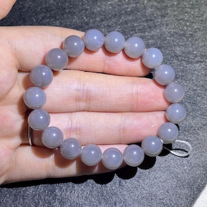 May include: A stretch bracelet composed of smooth, round, semi-translucent grey beads. The beads have a polished finish and are strung together on an elastic cord, forming a circular loop that fits around the wrist.