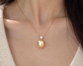 Könnte beinhalten: Eine goldene Kette mit einem einzelnen, großen, runden, goldfarbenen Perlenanhänger, der an einer kleinen, klaren, rund geschliffenen Edelsteinfassung hängt. Die zarte Kette besteht aus kleinen, gleichmäßigen Goldperlen.