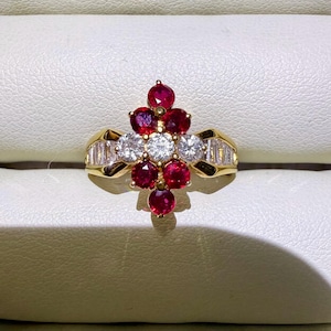 May include: A gold ring featuring a central cluster of five round red rubies and three round white diamonds, flanked by baguette-cut diamonds on each side of the band. The design is arranged in a vertical, diamond-like pattern on the gold setting.