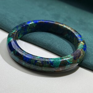 May include: A polished, round bracelet with a marbled appearance. The bracelet features a blend of blue, green, and brown hues. The gemstone bracelet is a piece of jewelry.