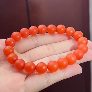 May include: A stretch bracelet composed of numerous round, matte-finish beads in a vibrant, solid orange colour. The beads are uniform in size and shape, strung together in a continuous circular loop to form a simple, minimalist piece of jewellery.
