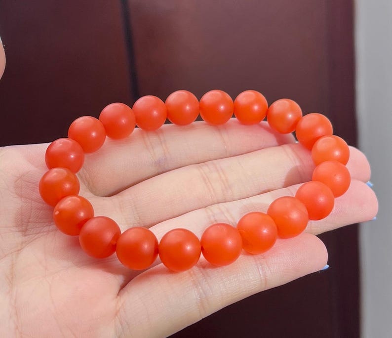 May include: A stretch bracelet composed of numerous round, matte-finish beads in a vibrant, solid orange colour. The beads are uniform in size and shape, strung together in a continuous circular loop to form a simple, minimalist piece of jewellery.