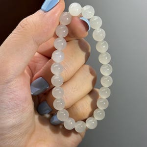 K&ouml;nnte beinhalten: Ein elastisches Armband bestehend aus glatten, runden, halbtransparenten wei&szlig;en Perlen. Die Perlen haben eine polierte Oberfl&auml;che und sind zu einer kreisf&ouml;rmigen Schlaufe aufgereiht, was ein schlichtes und gleichm&auml;&szlig;iges Design ergibt.