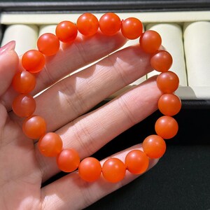 May include: A stretch bracelet composed of round, matte-finish orange beads. The beads are uniform in size and shape, strung together on an elastic cord to form a circular loop. The surface of each bead has a smooth, semi-translucent appearance.