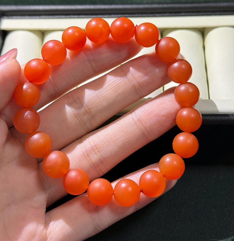 May include: A stretch bracelet composed of round, matte-finish orange beads. The beads are uniform in size and shape, strung together on an elastic cord to form a circular loop. The surface of each bead has a smooth, semi-translucent appearance.