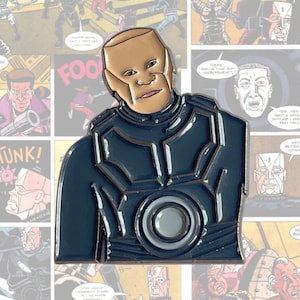 May include: A blue and grey enamel pin featuring a character with a bald head and a serious expression. The character is wearing a dark blue suit with a large, circular emblem on the chest.