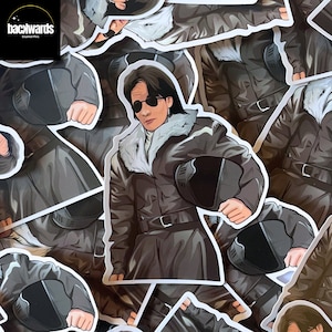 May include: A sticker featuring a cartoon illustration of a person wearing a brown leather jacket with a fur collar and a black helmet. The person is holding the helmet in their right hand. The sticker has a white border and the text "backwards" in a black box at the top left corner.