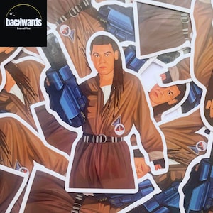 May include: A set of enamel pins featuring a character from a science fiction television show. The character is wearing a brown jumpsuit with a blue utility belt and a blue gun. The character has long brown hair and is holding the gun in their right hand. The pins are part of a collection of enamel pins featuring characters from the show.