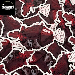 May include: A pile of red and white stickers with a spaceship design. The stickers have a white border and the text "RED DWARF" is visible on the side of the ship. The stickers are scattered across a surface.