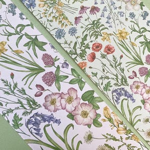 Op de afbeelding: Een witte achtergrond met een herhalend patroon van groene bladeren en verschillende bloemen in tinten roze, rood, geel, blauw en paars. De bloemen zijn willekeurig gerangschikt en worden omringd door groene bladeren.