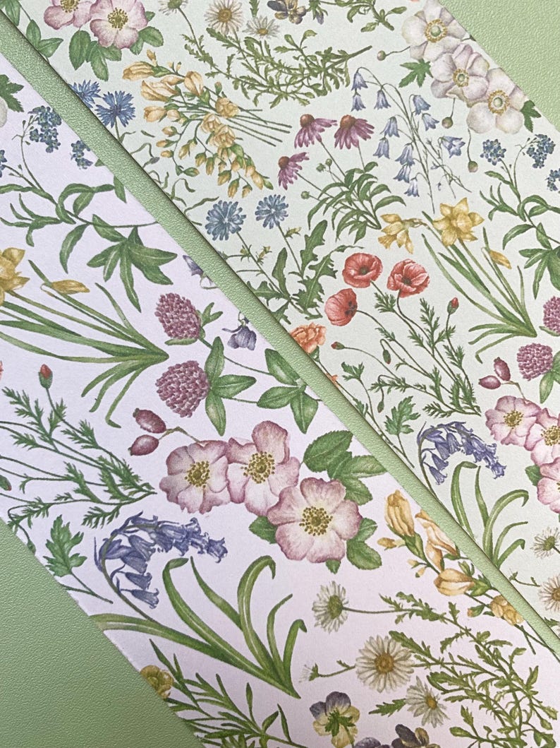 Op de afbeelding: Een witte achtergrond met een herhalend patroon van groene bladeren en verschillende bloemen in tinten roze, rood, geel, blauw en paars. De bloemen zijn willekeurig gerangschikt en worden omringd door groene bladeren.