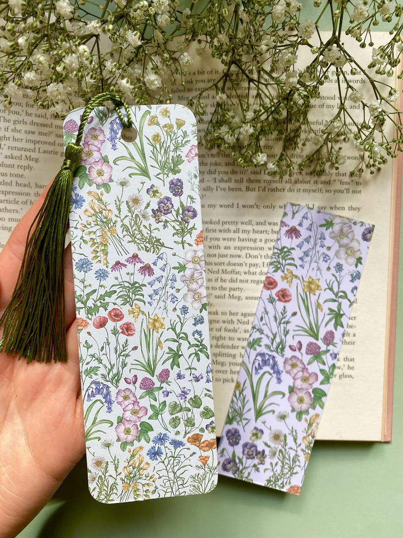 Op de afbeelding: Twee bloemen-bladwijzers met een groene kwast. De bladwijzers hebben een witte achtergrond met een verscheidenheid aan kleurrijke bloemen en groen.
