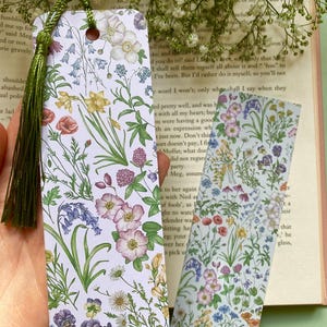 Op de afbeelding: Twee bloemen-bladwijzers met een witte achtergrond en een verscheidenheid aan kleurrijke bloemen, waaronder blauwe bellen, viooltjes en rozen.