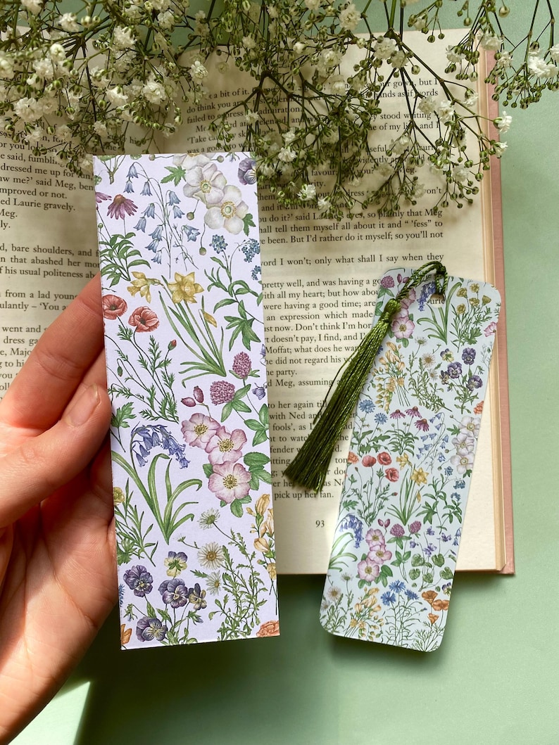 Op de afbeelding: Twee bloemen-bladwijzers met een witte achtergrond en kleurrijke bloemen. De bladwijzers zijn rechthoekig en hebben een groene kwast aan de rechterkant.
