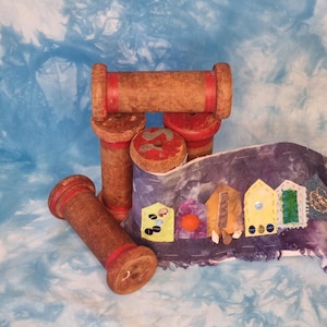 May include: A collection of wooden spools, each with red detailing, alongside a decorative textile with stitched-on, colourful embellishments. The spools are arranged in a still-life composition. The textile has a tie-dye effect.