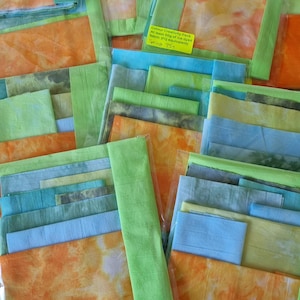 May include: A selection of fabric squares in various colours, including orange, green, and blue. Some are packaged in clear plastic. A yellow label reads "Colour Creativity Pack At least 50g of ice dyed fabric (FQ equivalent) Sp 759."