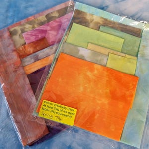 May include: Two sealed packs of colourful fabric squares. One pack features orange, green, and blue hues, while the other showcases pink, purple, and orange tones. A yellow label reads "Colour Creativity Pack" and "Spring 79g".