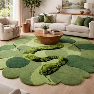 Op de afbeelding: Een groen vloerkleed met een slangenontwerp. Het vloerkleed heeft verschillende groentinten en een gedetailleerd slangenpatroon. Het vloerkleed ligt in een woonkamer met een witte bank en een houten salontafel.