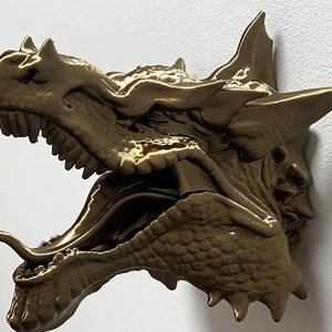 May include: A gold-coloured dragon head sculpture with an open mouth and a long tongue. The sculpture is detailed with scales and teeth.
