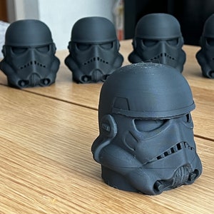 Op de afbeelding: Zes zwarte plastic Star Wars Stormtrooper-helmen op een houten tafel. De helmen zijn allemaal naar voren gericht en zijn in een rij gerangschikt.