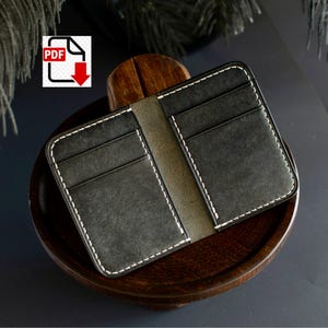 May include: Open black leather wallet with white stitching. The wallet has multiple card slots and a central compartment. The PDF download icon is in the upper left corner. The wallet is displayed on a wooden tray.