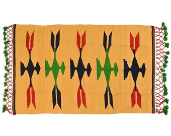 Puede incluir: Una alfombra amarilla con un patrón geométrico en rojo, verde y negro. La alfombra tiene flecos en los extremos.
