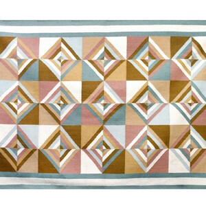 May include: A geometric patterned rug with a white background and a border of light blue. The rug features a repeating pattern of squares with overlapping triangles in shades of brown, pink, and blue.