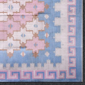 May include: A section of a patterned rug with a geometric design. The rug features a light blue, pink, and white colour scheme. The border has a Greek key pattern in pink and blue.