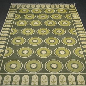 May include: A green and cream patterned rug with a repeating circle design. The rug has a fringed border.