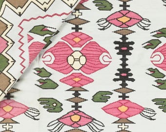 Puede incluir: Tela blanca con un patrón repetido de formas geométricas rosas, verdes, marrones y negras. El patrón presenta flores y hojas estilizadas.